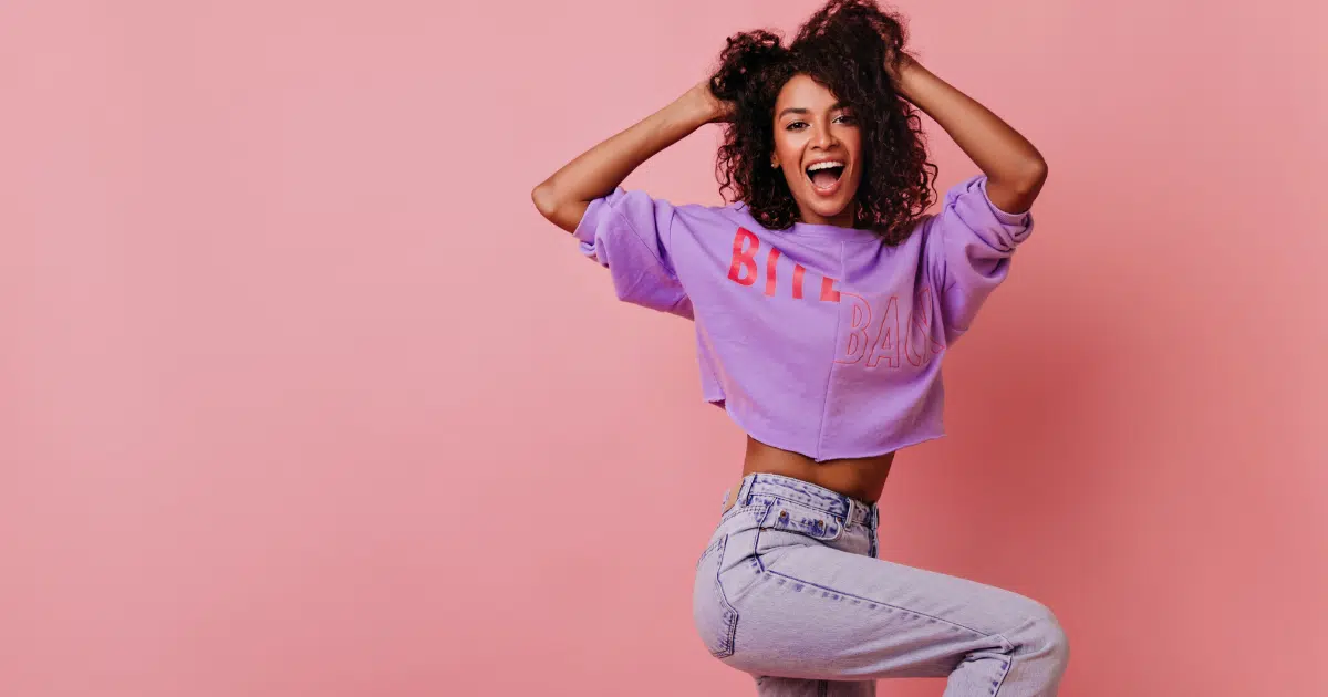 a woman with curly hair holding a joyful expression while sporting purple jeans and a shirt