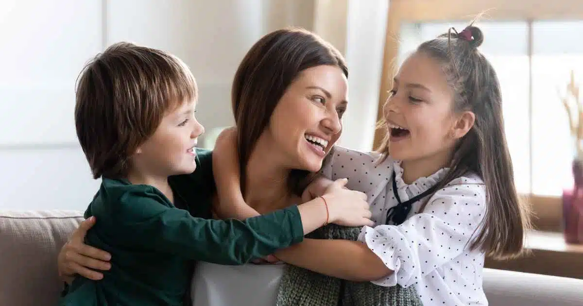 A mom with kids smiling while sitting in the sofa.