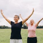 Two older women exercising outdoors in a grassy field