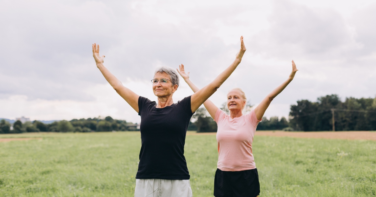 Two older women exercising outdoors in a grassy field