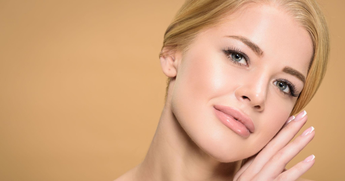 Close-up of a woman with clear skin gently touching her face against a soft beige background.