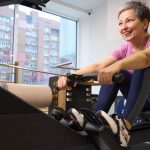 Smiling woman over 50 exercising on a rowing machine in a modern gym.